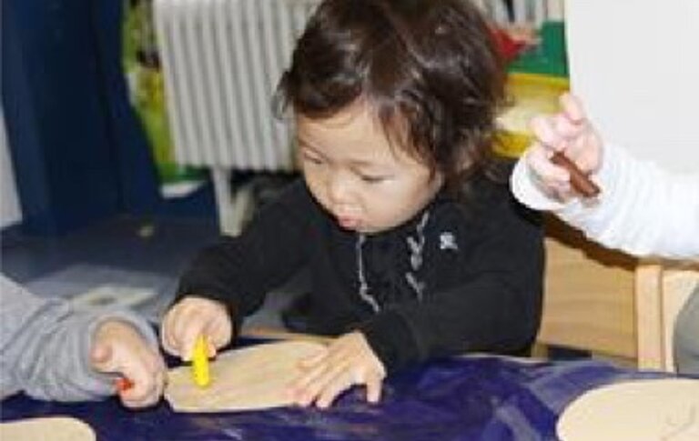 Kind welches mit Kreidestift auf einem Tisch malt